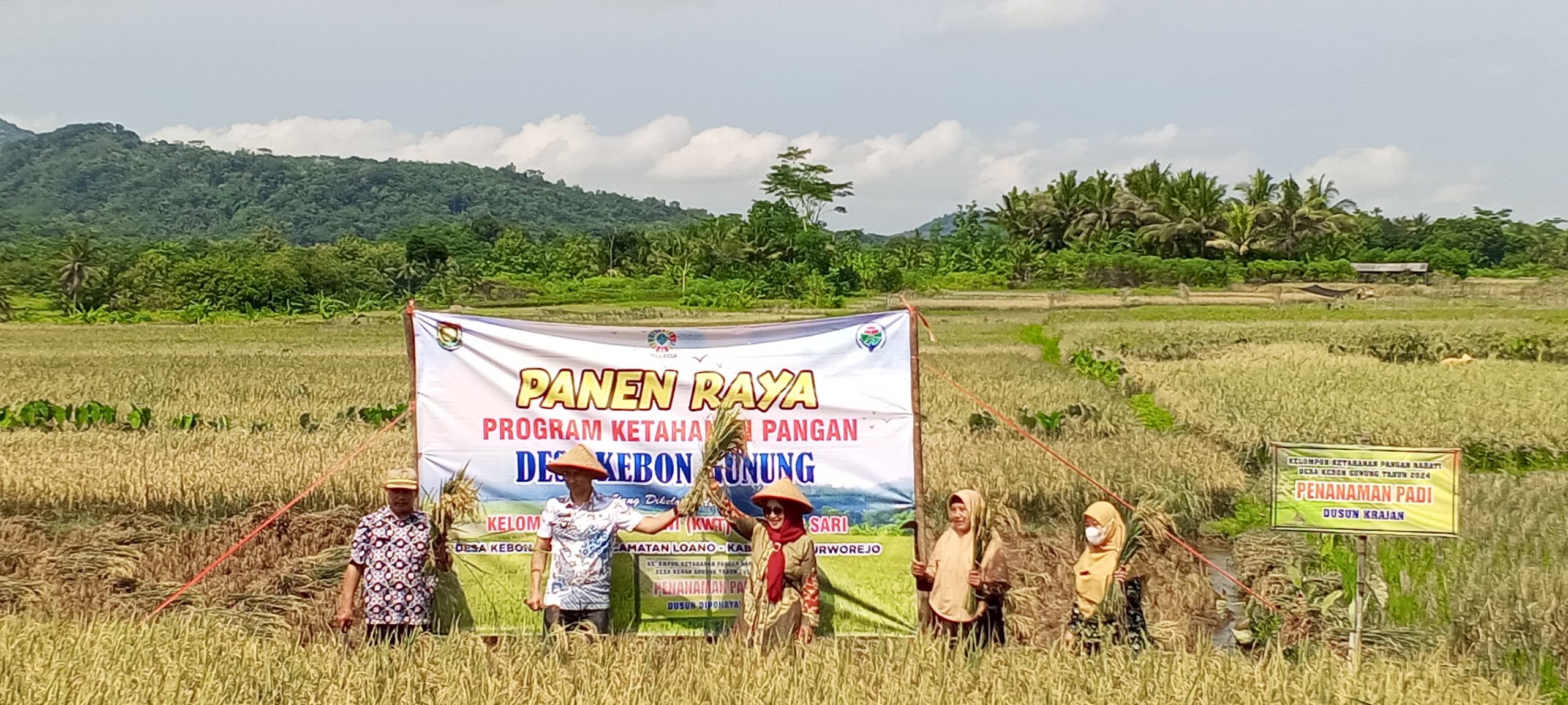 Foto Perangkat Desa Kedungdowo sedang menyerahkan secara simbolis karung bibit padi kepada perwakilan petani di balai desa, dengan latar belakang spanduk program ketahanan pangan